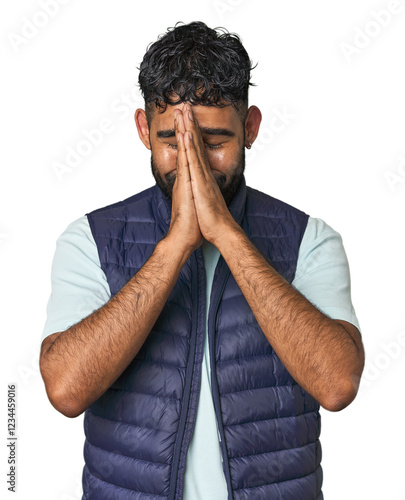 Young Hispanic man isolated holding hands in pray near mouth, feels confident. photo