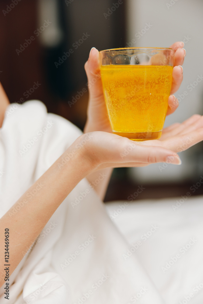 Woman holding glass of orange juice while laying in bed with white sheet Woman holding glass of orange juice while laying in bed with white sheet
