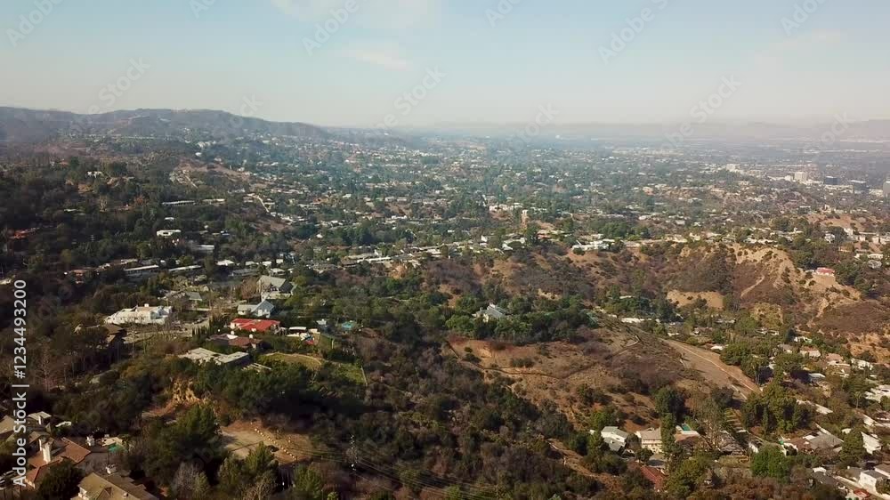 Aerial establishing shot San Fernando Valley with luxury homes and tennis field on top of hill. Sunny day with foggy landscape. Los Angeles County, California, USA. Drone wide shot.