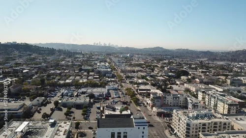 Suburb City with traffic on main street and Skyline of Los Angeles behind mountains in distance. Aerial panning wide shot. Historic buildings and apartments in Glendale City at sunset. photo