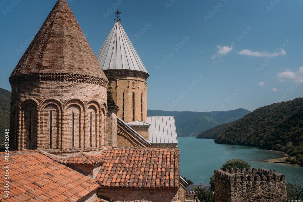 Obraz premium Ananuri Fortress and Zhinvali Reservoir in Georgia. Ancient stone fortress with conical towers and tiled roofs overlooking a blue mountain lake. Green hills in the background. Historic landmark