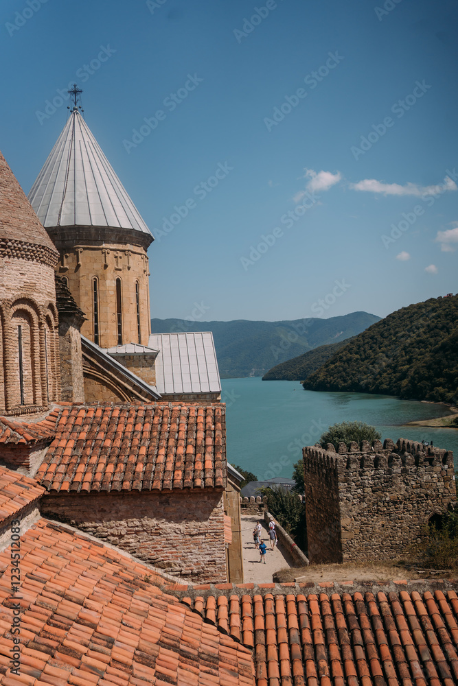 Obraz premium Ananuri Fortress and Zhinvali Reservoir in Georgia. Ancient stone fortress with conical towers and tiled roofs overlooking a blue mountain lake. Green hills in the background. Historic landmark