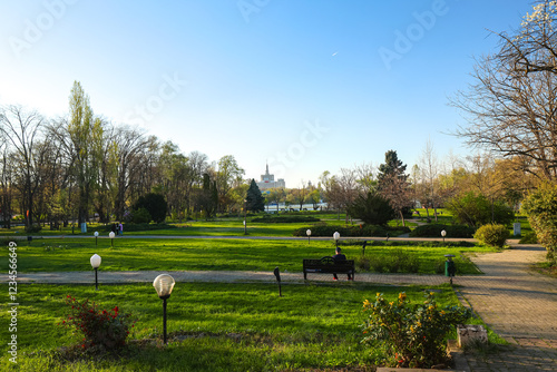 Obraz na płótnie A peaceful park view in Bucharest during springtime, with lush green lawns, blooming trees, and a serene lake reflecting the clear blue sky. An ideal spot for relaxation. Herastrau King Michael I park w salonie