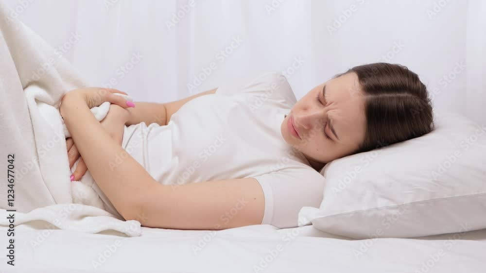 A slender, beautiful woman is holding her stomach in her bed, her stomach hurts. A slender, beautiful woman is holding her stomach in her bed, her stomach hurts.