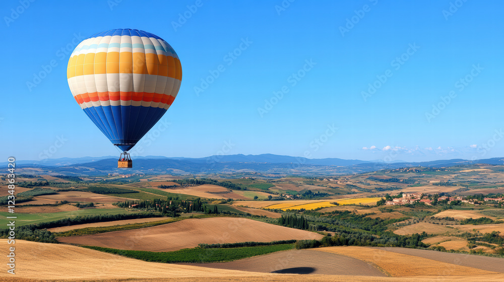 Obraz premium vintage style hot air balloon floats gracefully over picturesque landscape, showcasing rolling hills and vibrant fields under clear blue sky. scene evokes sense of adventure and tranquility