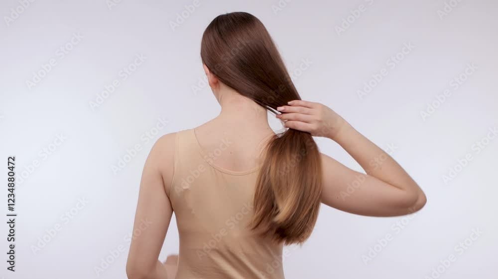 Young beautiful girl in a beige sweater with long hair. The girl combs her hair.