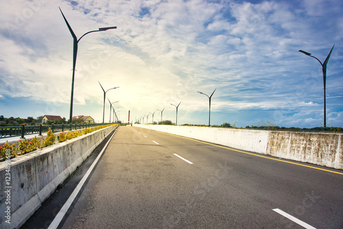 Sunlit road stretching into the horizon with decorative streetlights and vibrant green vegetation photo