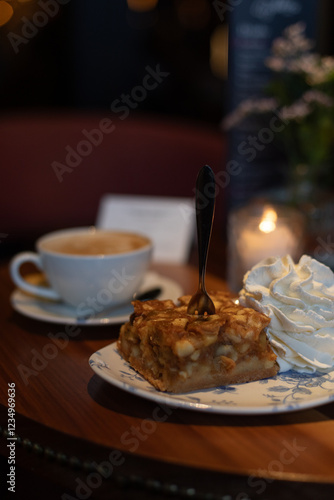 Piece of apple pie with whipped cream and a cup of cappuccino on a table in a restaurant 