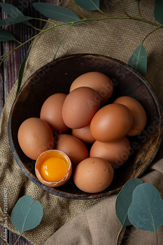 Brown chicken eggs in round wooden bowl, one egg is broken, perfect for Easter, natural light 