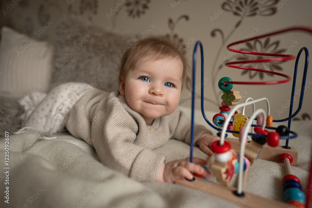 Naklejka premium Adorable 6-month baby playing with educational wooden toy on bed coat. Activity for motor and sensory development.