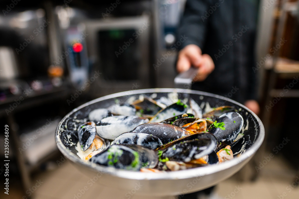 A chef presents a skillet of freshly cooked mussels garnished with herbs, showcasing vibrant seafood in a professional kitchen setting. Perfect for culinary themes and seafood recipes. A chef presents a skillet of freshly cooked mussels garnished with herbs, showcasing vibrant seafood in a professional kitchen setting. Perfect for culinary themes and seafood recipes.