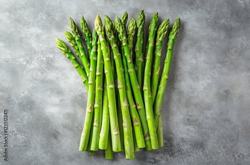 A bunch of fresh green asparagus is displayed against a subtle light gray background. The asparagus spears are vibrant and firm, highlighting their freshness and quality photo