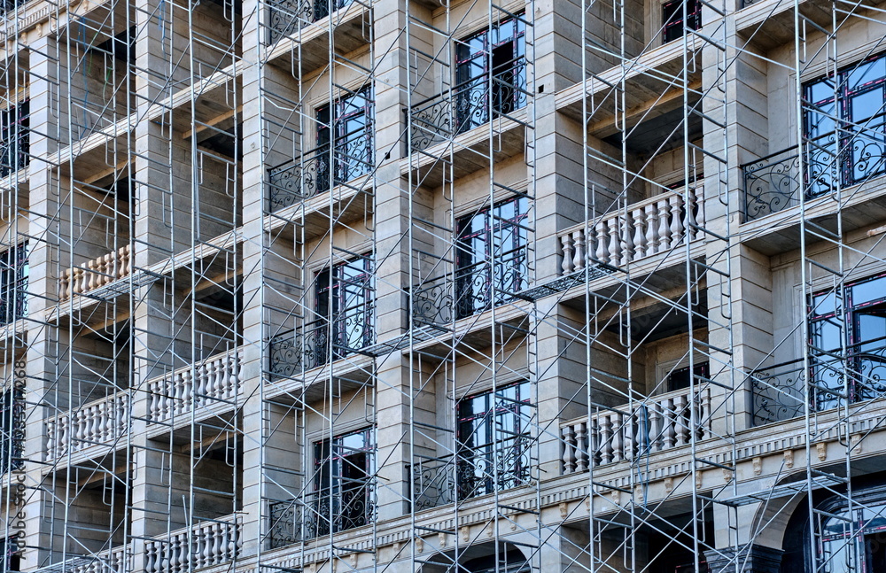 Facade of a multi-story building under construction with scaffolding and balconies. Facade of a multi-story building under construction with scaffolding and balconies.