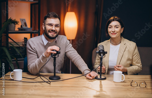 Professional podcast duo discussing content, speaking into microphones while seated in soundproofed recording studio environment photo