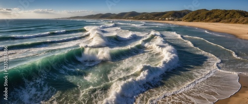 Ocean waves crashing on a sandy beach, creating a stunning display of nature's power and beauty. The sunlit water sparkles, showcasing the vibrant colors of the sea. photo