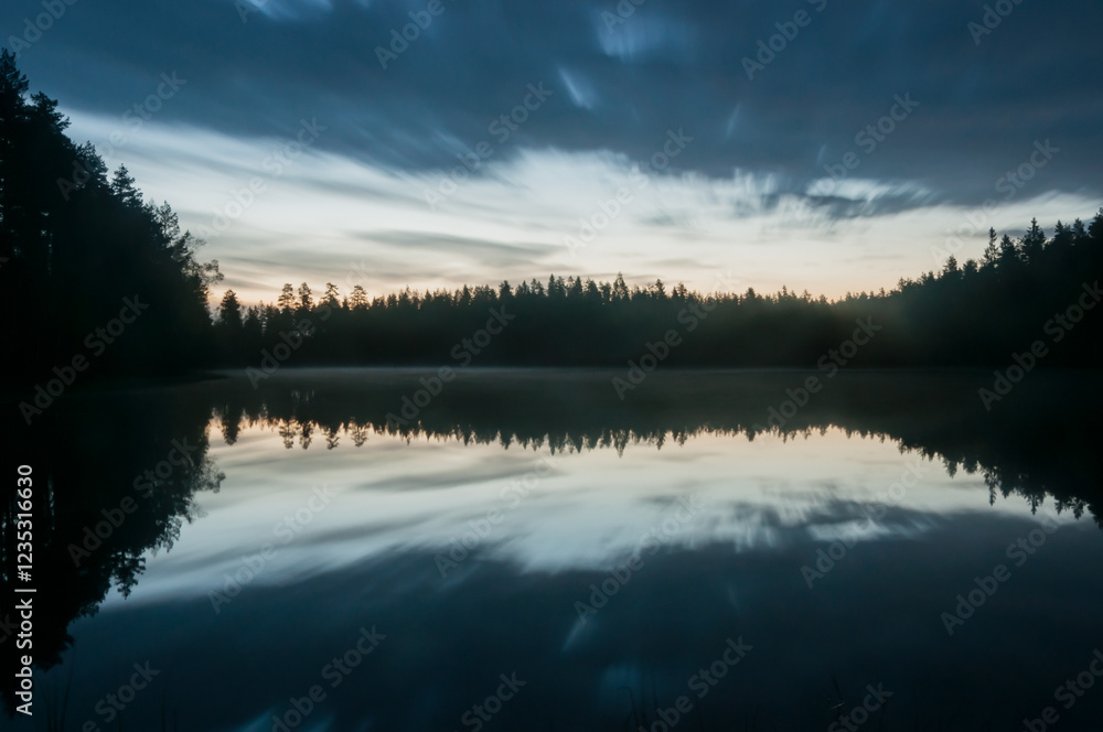 Fototapeta premium A scenic and calm lake view at night with mist and reflected forest on the surface in Finland