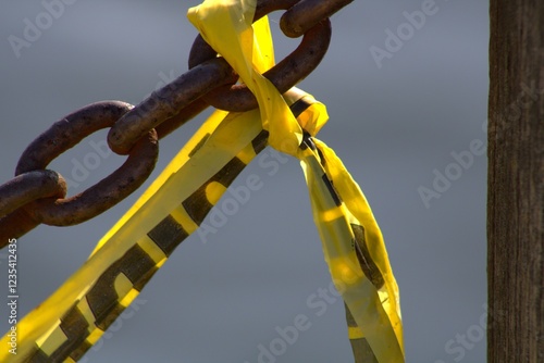 torn caution tape tied around rusted chain near water