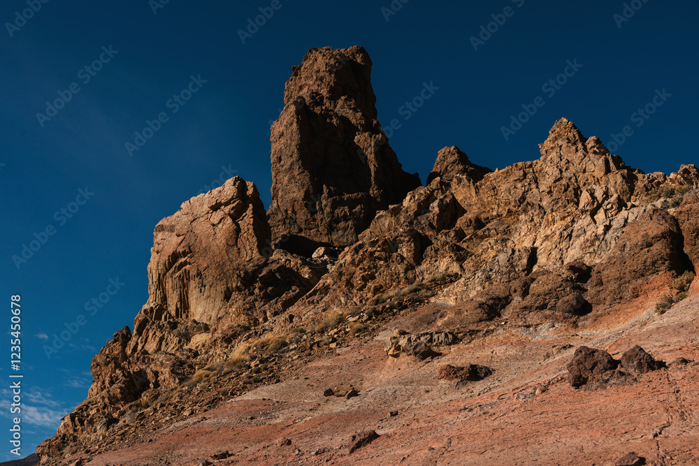 Fototapeta premium Massive rocky cliff with rugged textures and warm tones under a deep blue sky in a desert-like setting.
