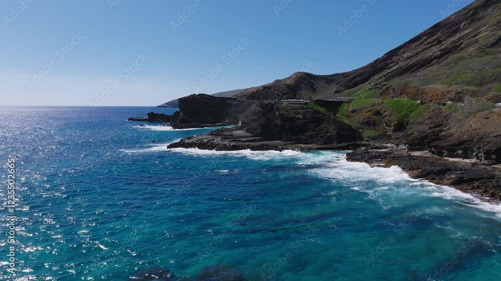 Aerial view of Oahu Island's coastline, featuring a rocky mountain ridge, ocean waves crashing on the shore, and a road with moving vehicles. Aerial view of Oahu Island's coastline, featuring a rocky mountain ridge, ocean waves crashing on the shore, and a road with moving vehicles.
