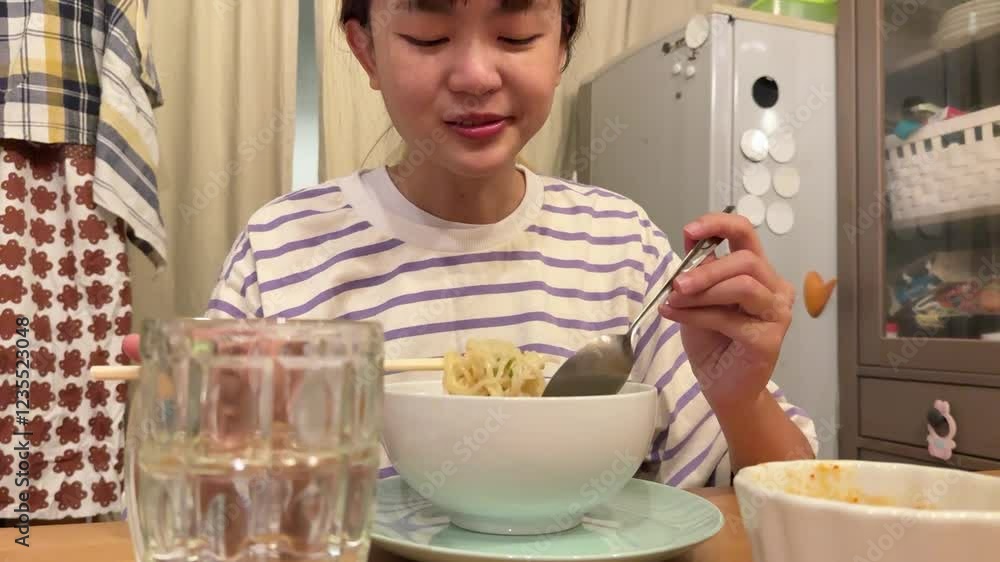 The young East Asian woman is eating instant noodles with sukiyaki sauce soup at home alone during the night. The young East Asian woman is eating instant noodles with sukiyaki sauce soup at home alone during the night.