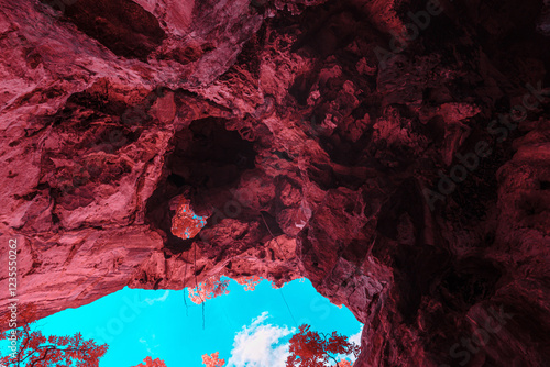 Infrared techniques, a stunning view from within a cave, looking up towards the sky. The cave ceiling is made of rough, textured rock, painted in a deep of red