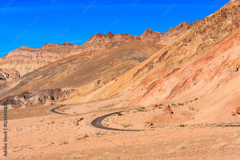 Naklejka premium A road winds through a desert with a blue sky in the background