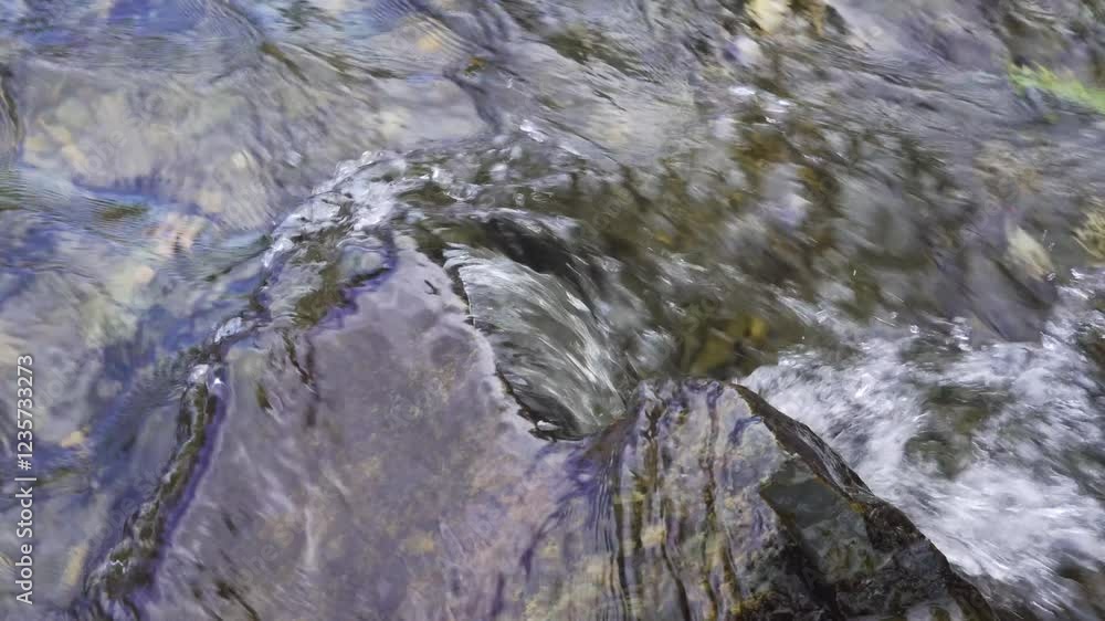 Close up on a lime stone in the middle of a river with crystal clear water flowing. Water flowing down stream covering the lime stone and creating some wave movement and water splash. 4K 60fps. Close up on a lime stone in the middle of a river with crystal clear water flowing. Water flowing down stream covering the lime stone and creating some wave movement and water splash. 4K 60fps.