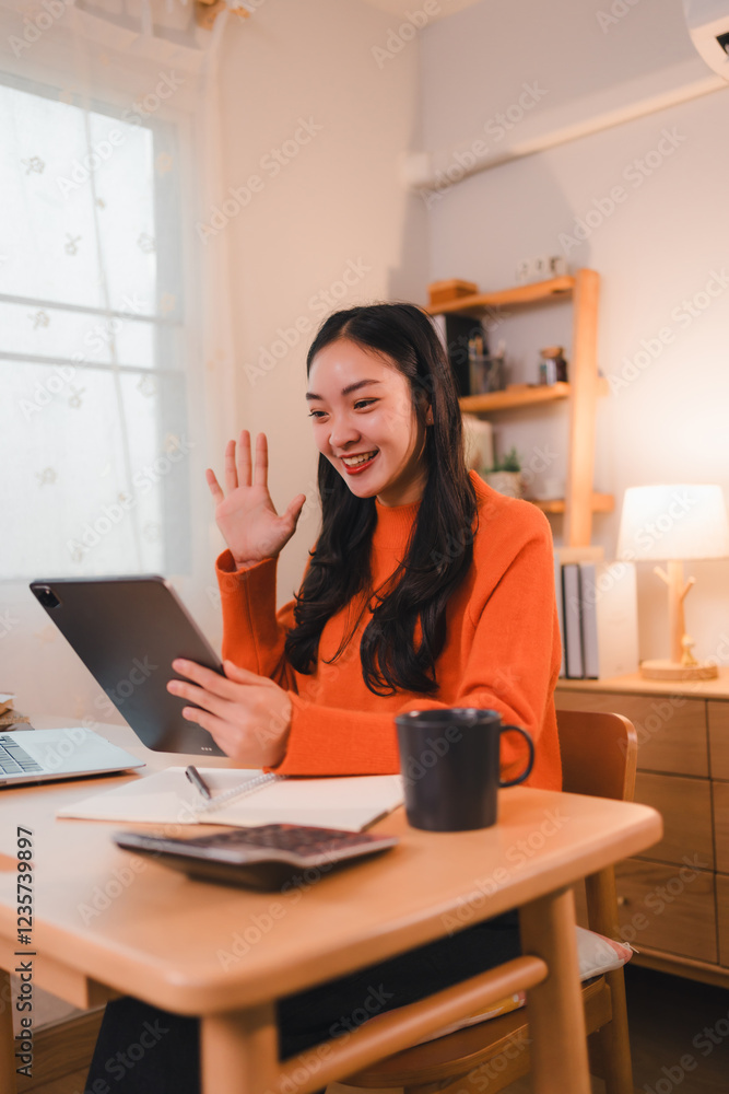 woman in orange sweater smiling and waving during video call at cozy home office woman in orange sweater smiling and waving during video call at cozy home office