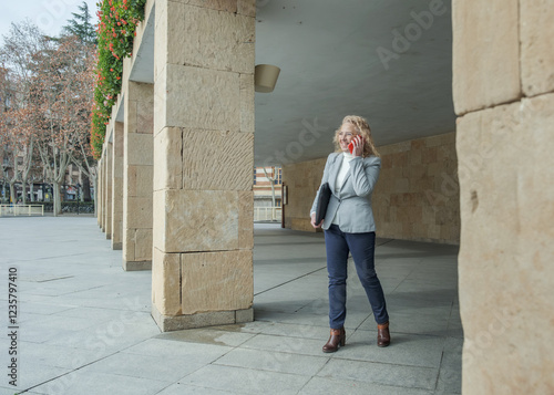 Businesswoman walking and talking on the phone under a portico photo