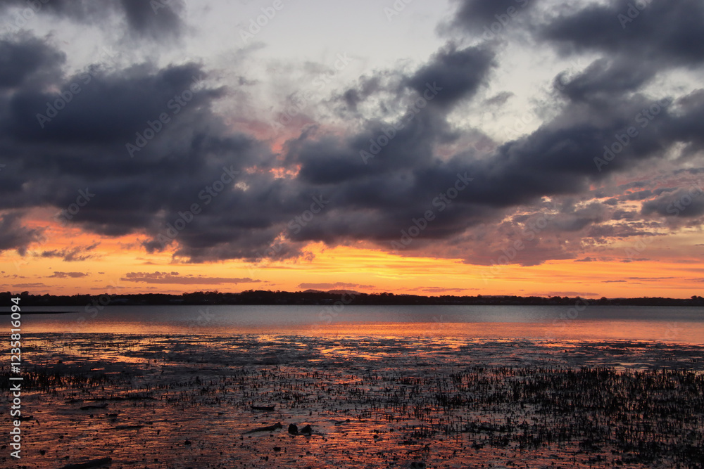 Fototapeta premium Dramatic sunset over a calm bay with a vibrant orange and purple sky