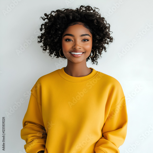 Smiling young woman with curly hair wearing a mustard yellow sweatshirt, portrait of a happy and confident person