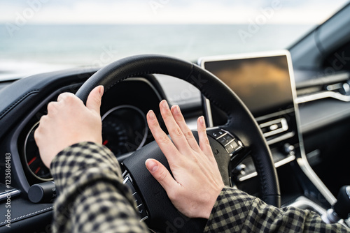 Woman hand pressing the horn button while driving an automobile. Female driver honking the car horn. Girl angry at the traffic jam ahead and using a car horn to attract attention on the road. Close up photo