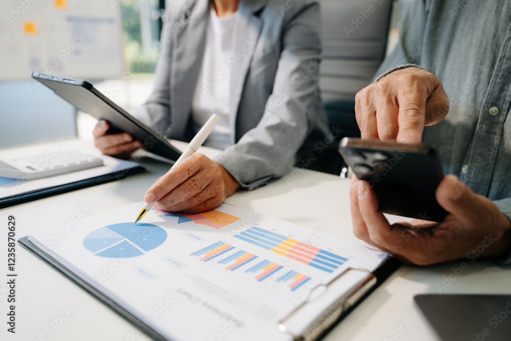 Business documents on office table with smart phone and laptop and two colleagues discussing data Business documents on office table with smart phone and laptop and two colleagues discussing data