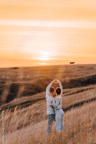 A romantic couple shows a heart sign against the sunset, a young couple's date in nature