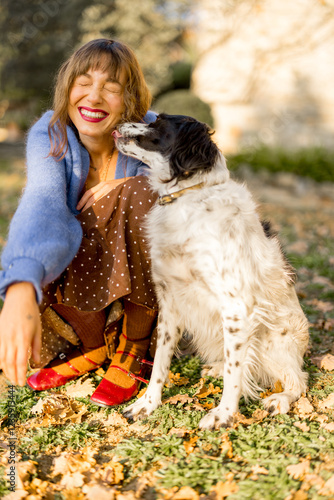 Canvas Print A cheerful woman with two dogs sitting in a sunny countryside setting near a rustic stone house