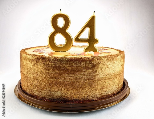 Decorated gold cake for birthday or anniversary party, candle number 84, white background photo