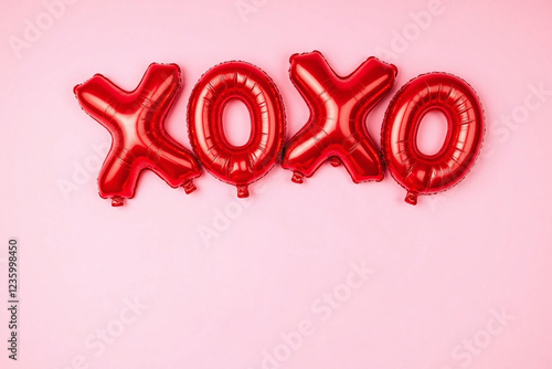 Red shiny balloons spell XOXO with heart shape below on pink photo