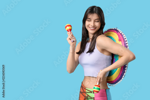 Young woman with colorful sombrero and maracas on blue background. Cinco de Mayo celebration