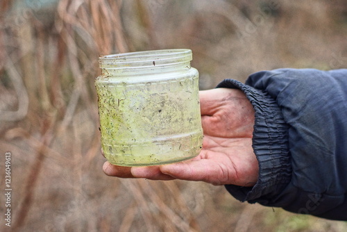 one glass canning jar discarded small empty dirty open round threaded gray transparent jar in hand of man daytime outdoors