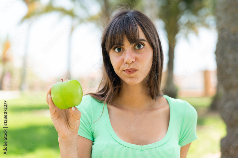 Young woman with an apple at outdoors with sad expression Young woman with an apple at outdoors with sad expression