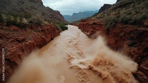Muddy river flooding through red rock canyon walls. Natural disaster background