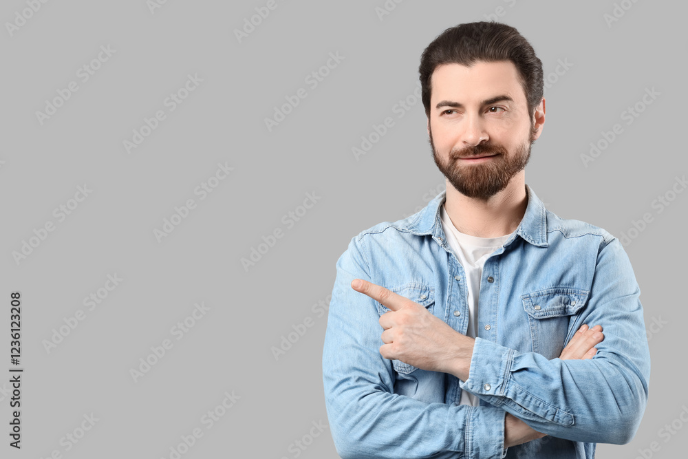 Bearded young man with crossed arms pointing at something on grey background Bearded young man with crossed arms pointing at something on grey background