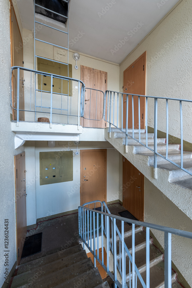 Obraz premium Empty Apartment Stairwell with Multiple Doors and Metal Railings. Brightly lit residential stairwell in an apartment building, showcasing doors, concrete stairs, and railings.