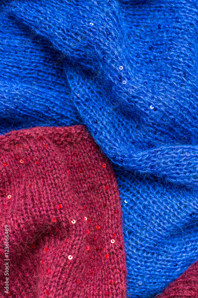 Red and blue knitted sweater with sequins. Sequinned knitwear. Sequin pattern in needlework. Knitting hobby. Knitter work. Sequins texture in knitwear. Bright knitted fashion for holidays.