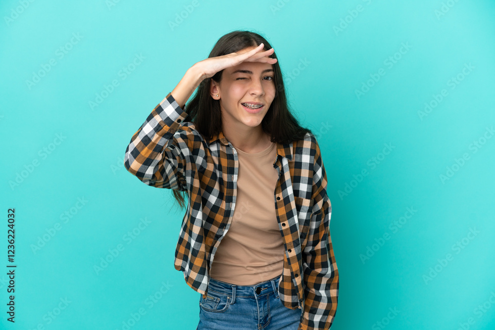 Young French woman isolated on blue background looking far away with hand to look something Young French woman isolated on blue background looking far away with hand to look something