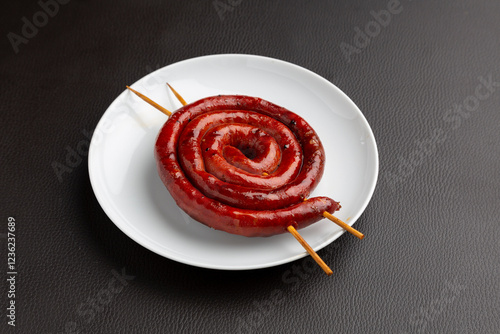 Spiral-coiled chistorra sausage grilling on wooden skewer, resting on pristine ceramic plate