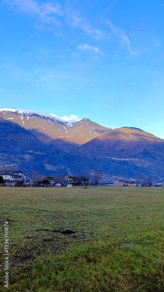 Naklejka premium Beautiful mountains against a blue sky. Houses at the foot of the mountains. Vertical image of majestic mountains.