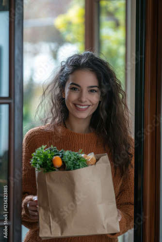 Happy latin woman receiving a food delivery order in a brown paper bag at the doorway of her home