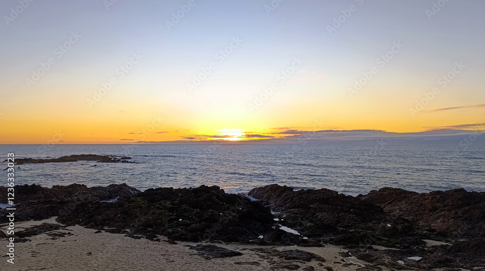 The ocean shore. The sun is sinking below the horizon in a blue sky. Beautiful sunset. Horizontal image. The ocean shore. The sun is sinking below the horizon in a blue sky. Beautiful sunset. Horizontal image.
