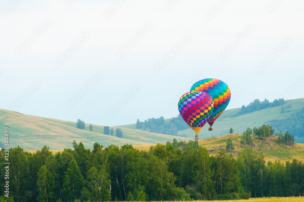 Colorful hot air balloons flying over the green hills and trees at sunset.